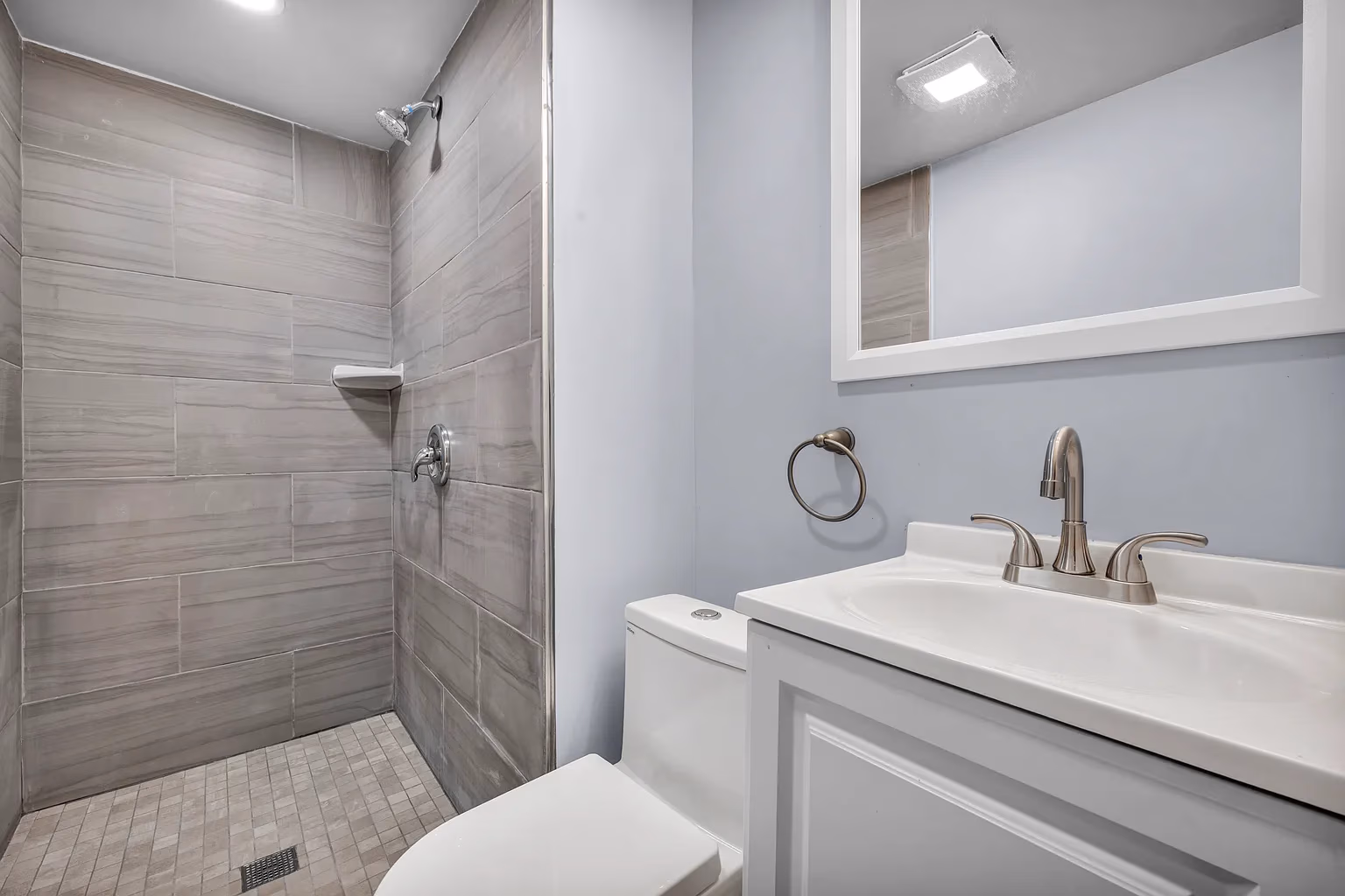 Modern bathroom with tiled walk-in shower, white toilet, and vanity with faucet and mirror.