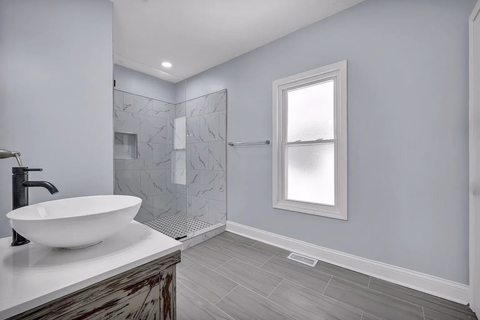 Modern bathroom with vessel sink, black faucet, walk-in shower with glass partition, and frosted window.