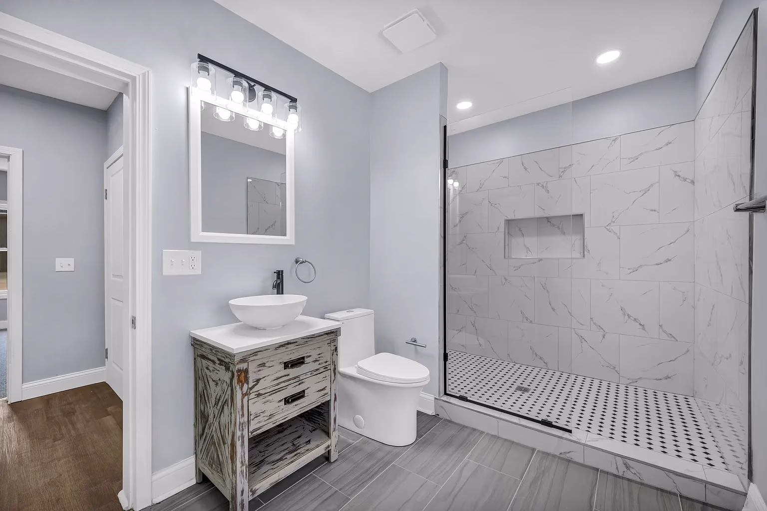 Modern bathroom with rustic vanity, vessel sink, toilet, and glass shower with marble tile walls.