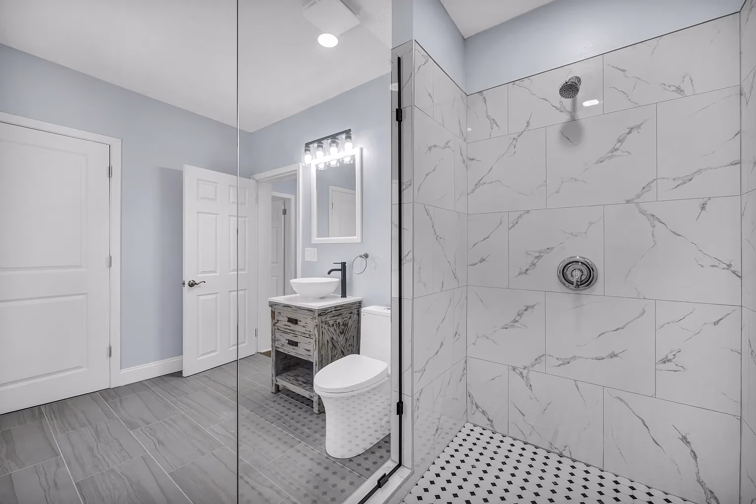 Modern bathroom with glass shower, marble tiled walls, white toilet, and rustic wooden vanity with vessel sink.