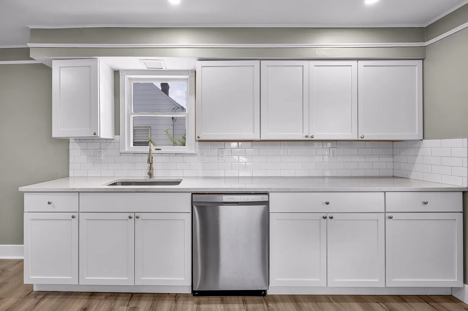 Modern kitchen with white cabinets, subway tile backsplash, stainless dishwasher, sink, and window.