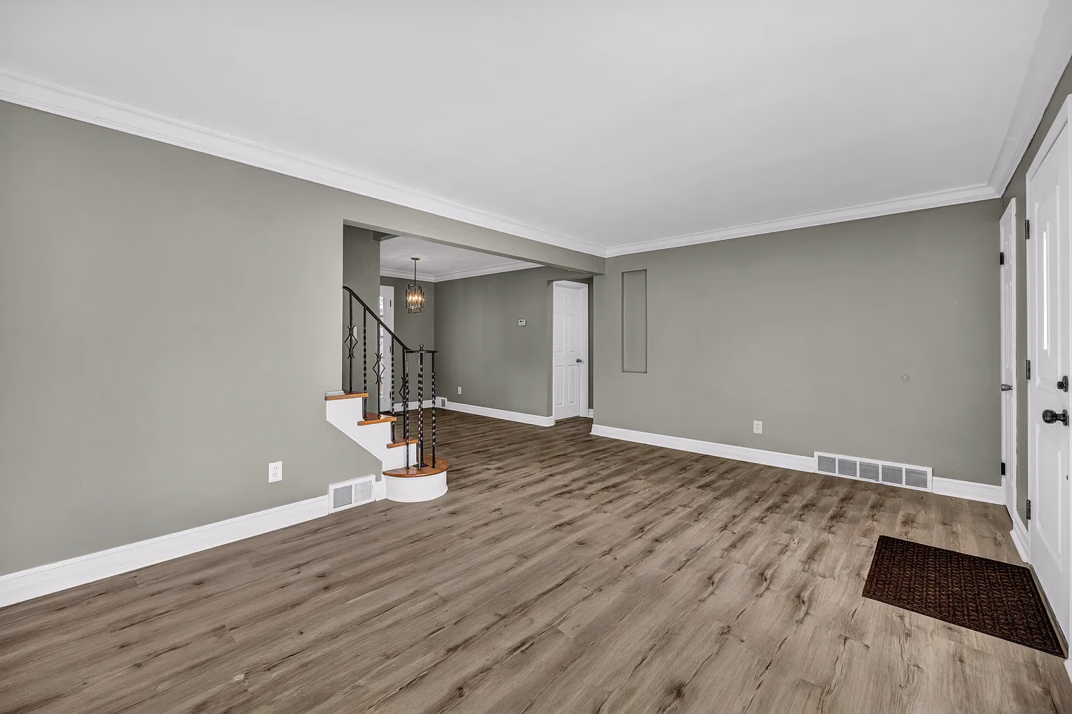 Empty room with light wood flooring, green-gray walls, white trim, stair railing, and white doors.