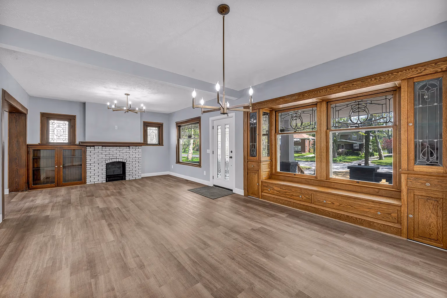 Empty living room with wood floors, a white brick fireplace, stained glass windows, and wood built-in seating.