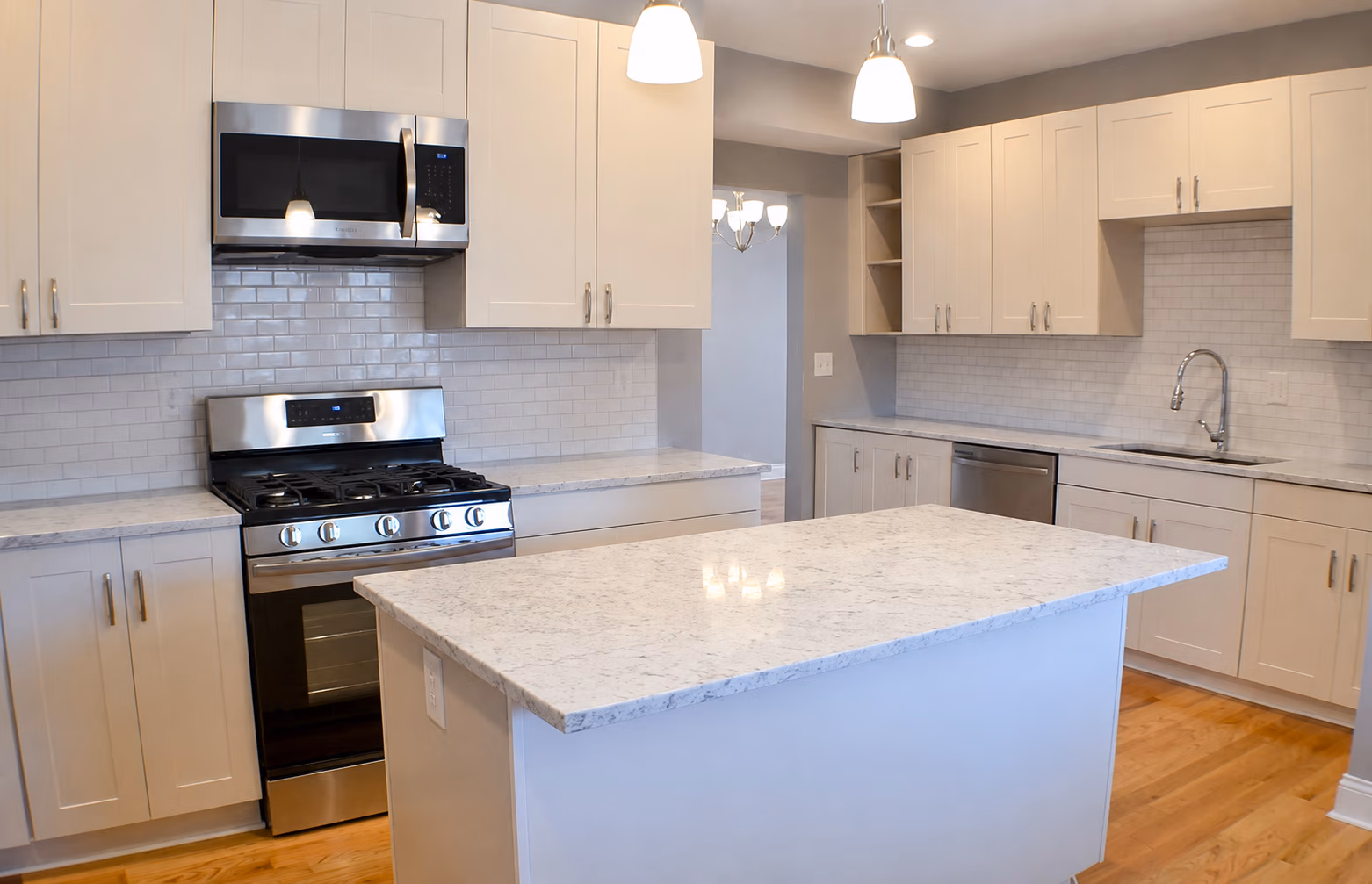 Modern kitchen with white cabinets, marble island, stainless steel stove, microwave, and dishwasher.