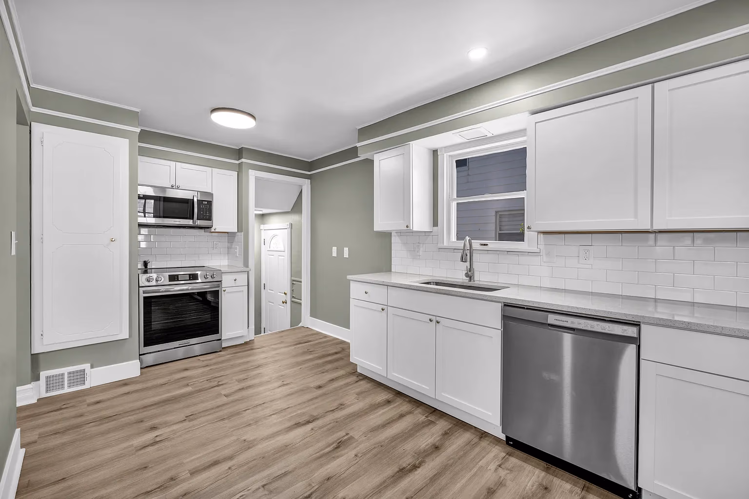 Modern kitchen with white cabinets, stainless steel appliances, subway tile backsplash, and wood flooring.