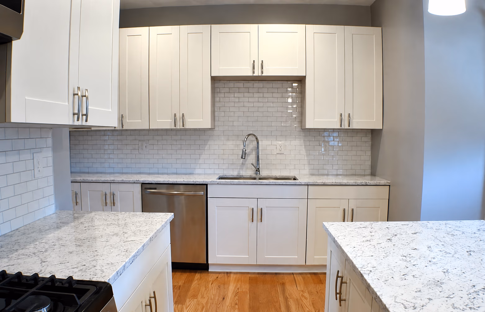 Modern kitchen with white cabinets, marble countertops, subway tile backsplash, and stainless steel sink.