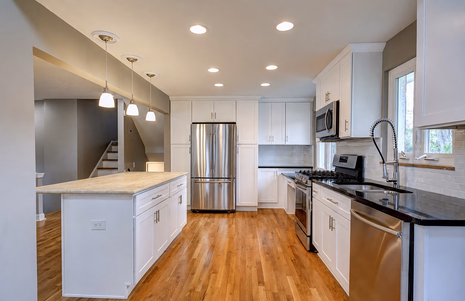 Modern kitchen with white cabinets, stainless steel appliances, hardwood floors, and pendant lighting.