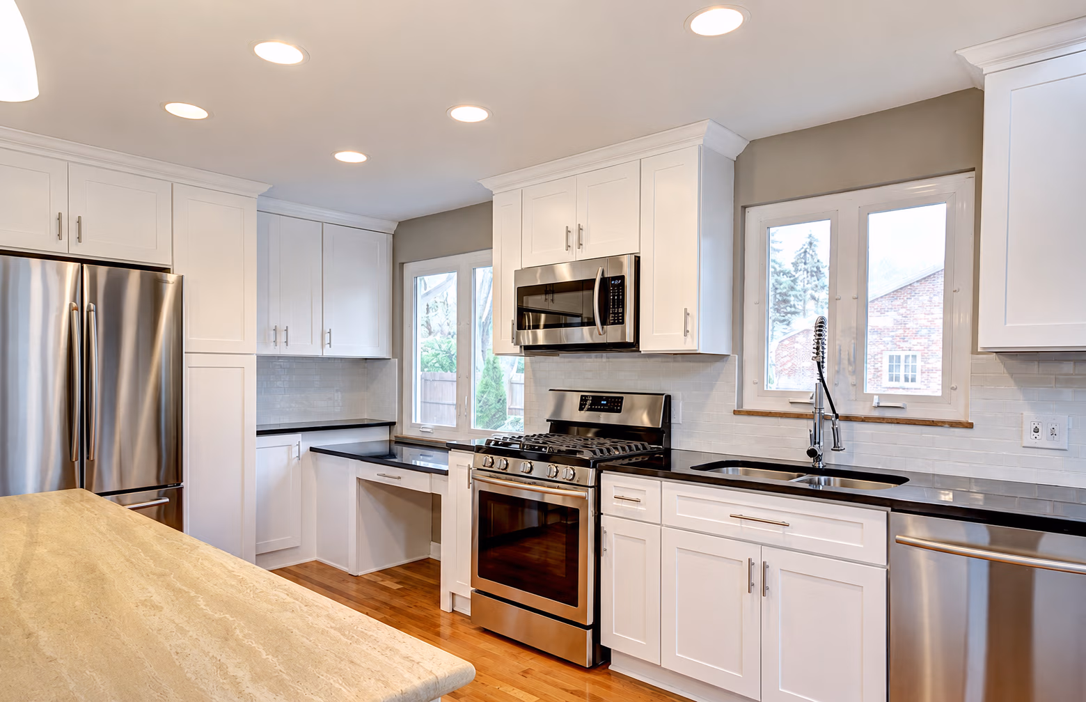 Modern kitchen with white cabinets, stainless steel appliances, black countertops, and wood floor.