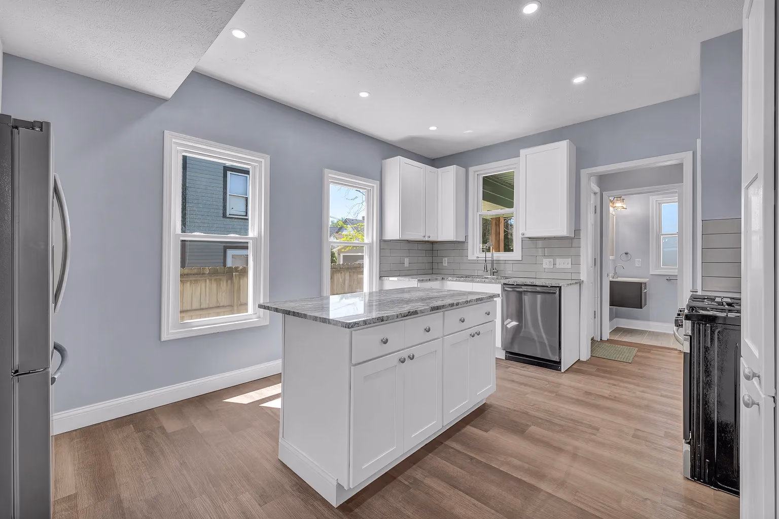Modern kitchen with white cabinets, marble island, stainless steel appliances, and light wood flooring.