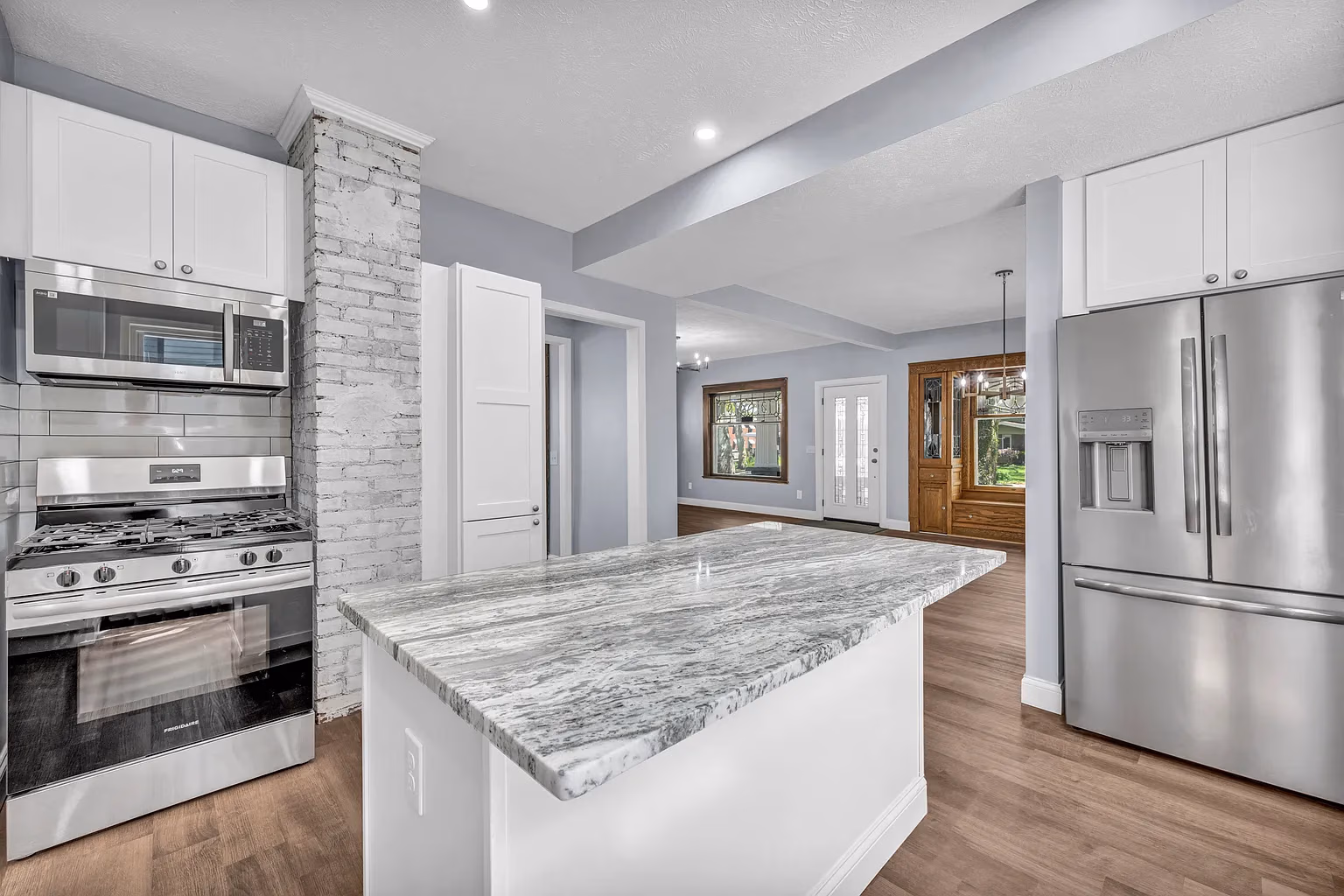 Modern kitchen with marble island, stainless steel stove, microwave, and refrigerator with hardwood floors.