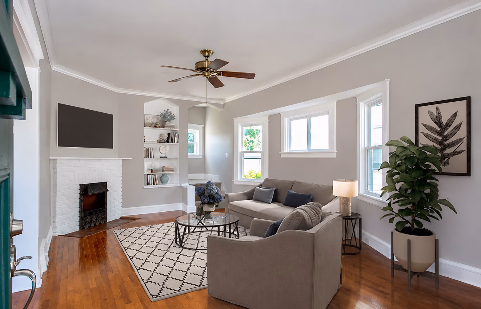 Living room with gray sofas, glass coffee table on patterned rug, white brick fireplace, and green plant by window.