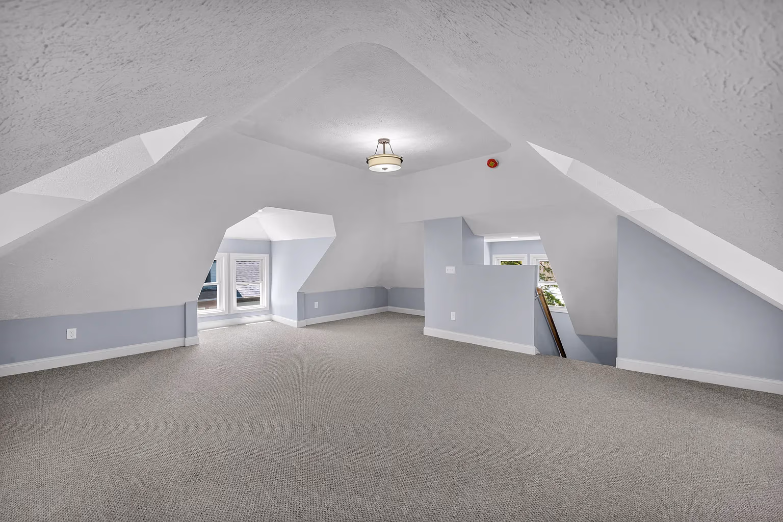 Empty attic room with light gray carpet, light blue walls, and a ceiling light fixture.