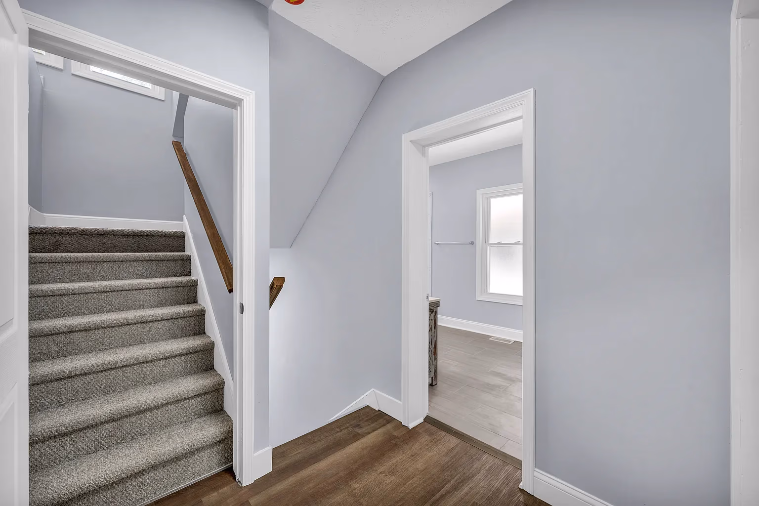Interior hallway with carpeted stairs on left and an open door leading to a room with a window on right.