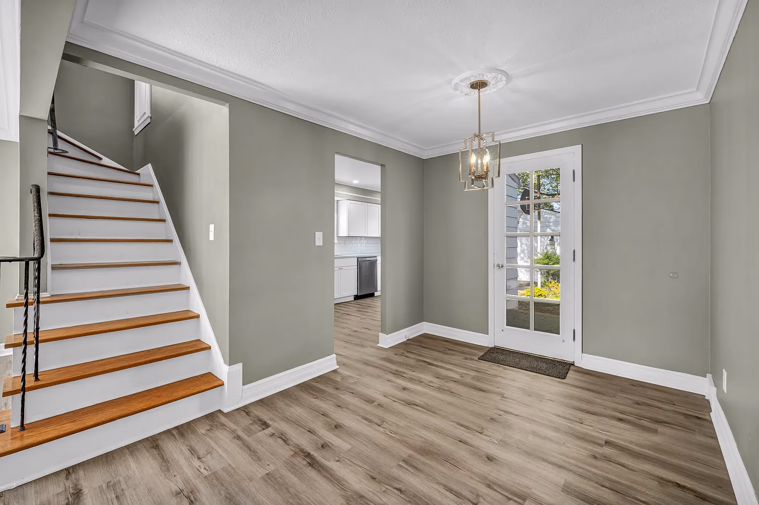 Empty room with wood flooring, gray walls, stairs on left, and glass door to outside on right.