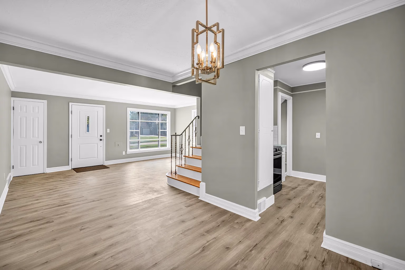 Empty living room with light wood floors, greenish walls, white trim, and stairs with wooden steps and iron railing.