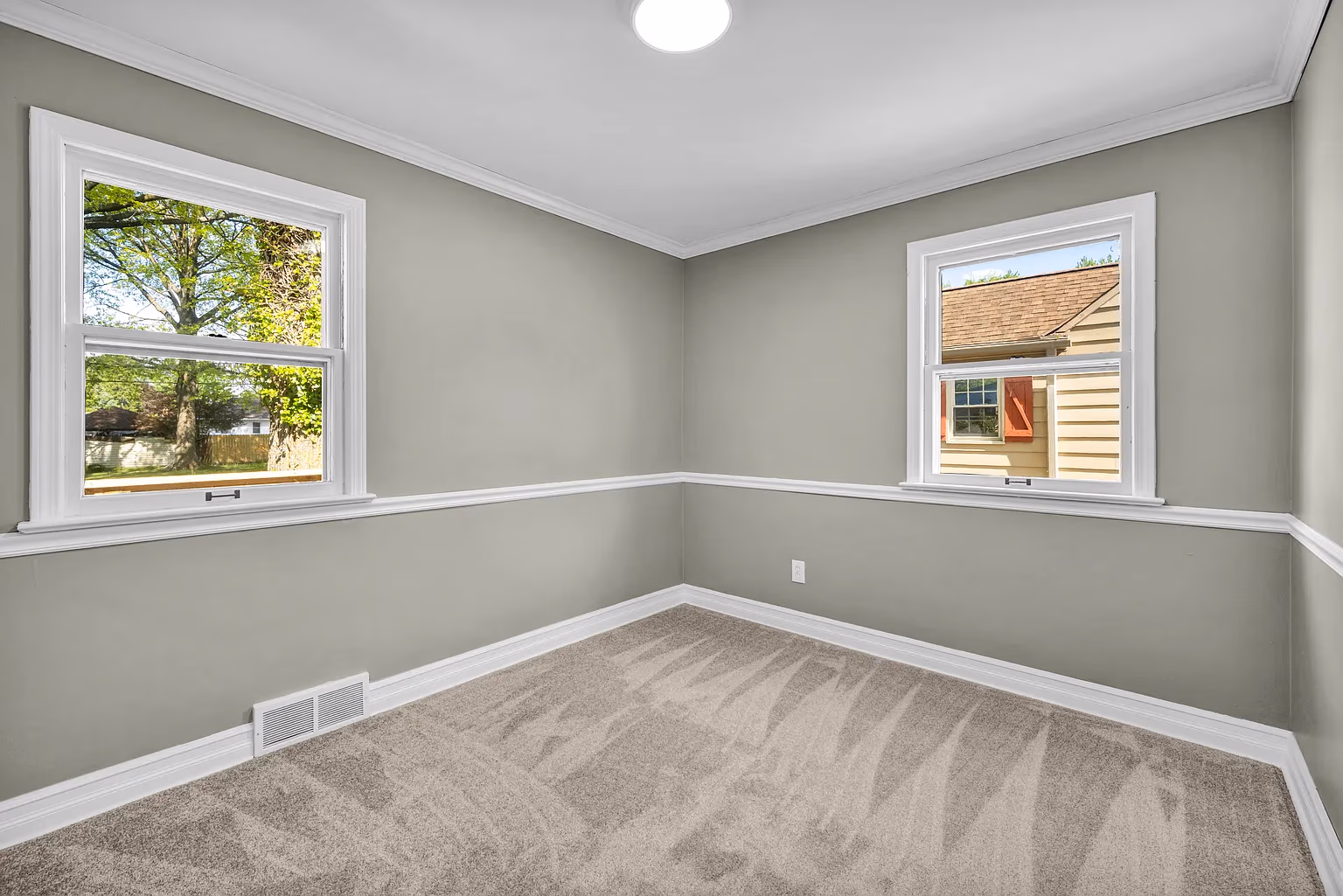 Empty room with light gray walls, two windows, white trim, and beige carpet with vacuum lines.