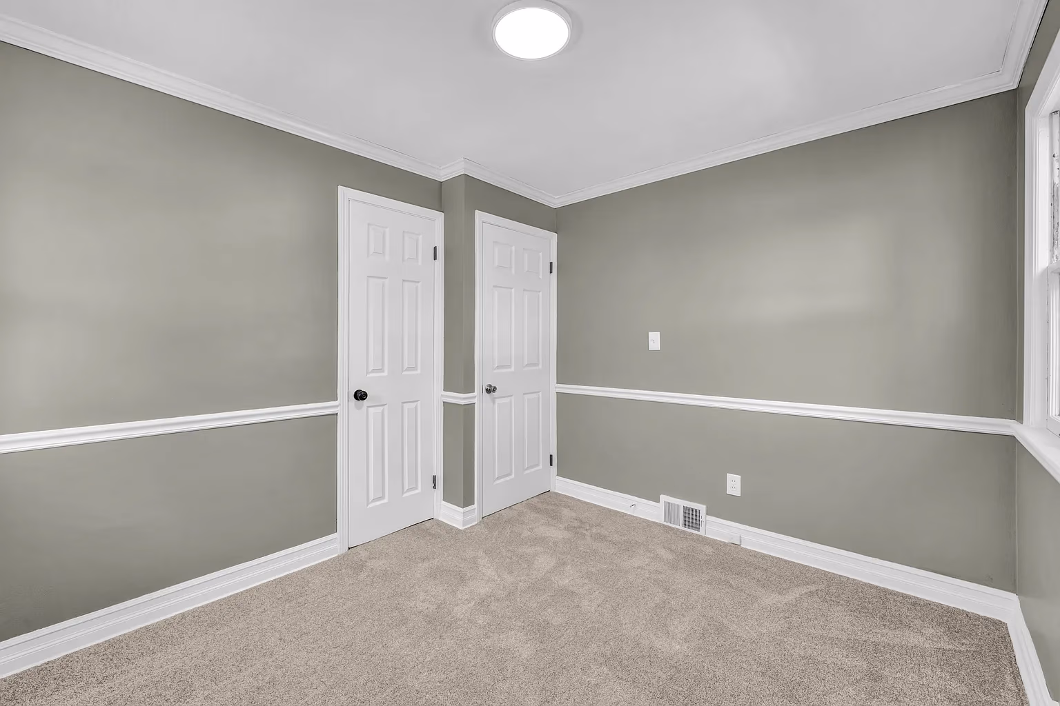 Empty room with gray walls, white doors, beige carpet, crown molding, and a window on the right.