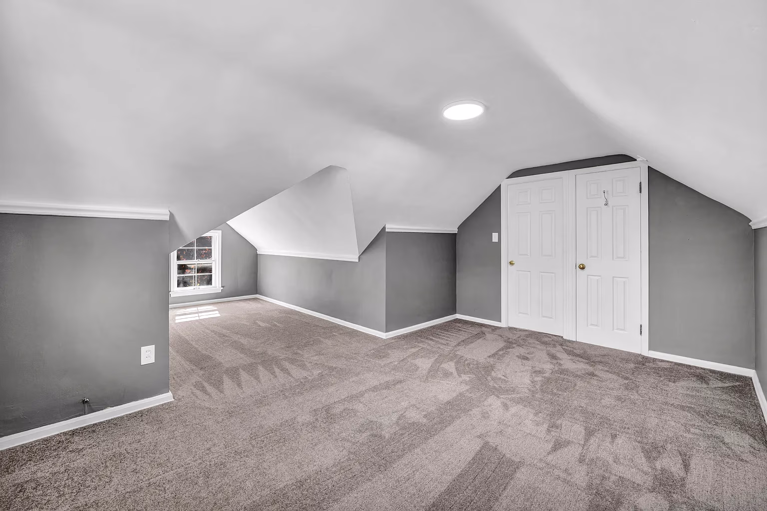 Empty room with gray walls, beige carpet, sloped ceiling, window, and white double doors.