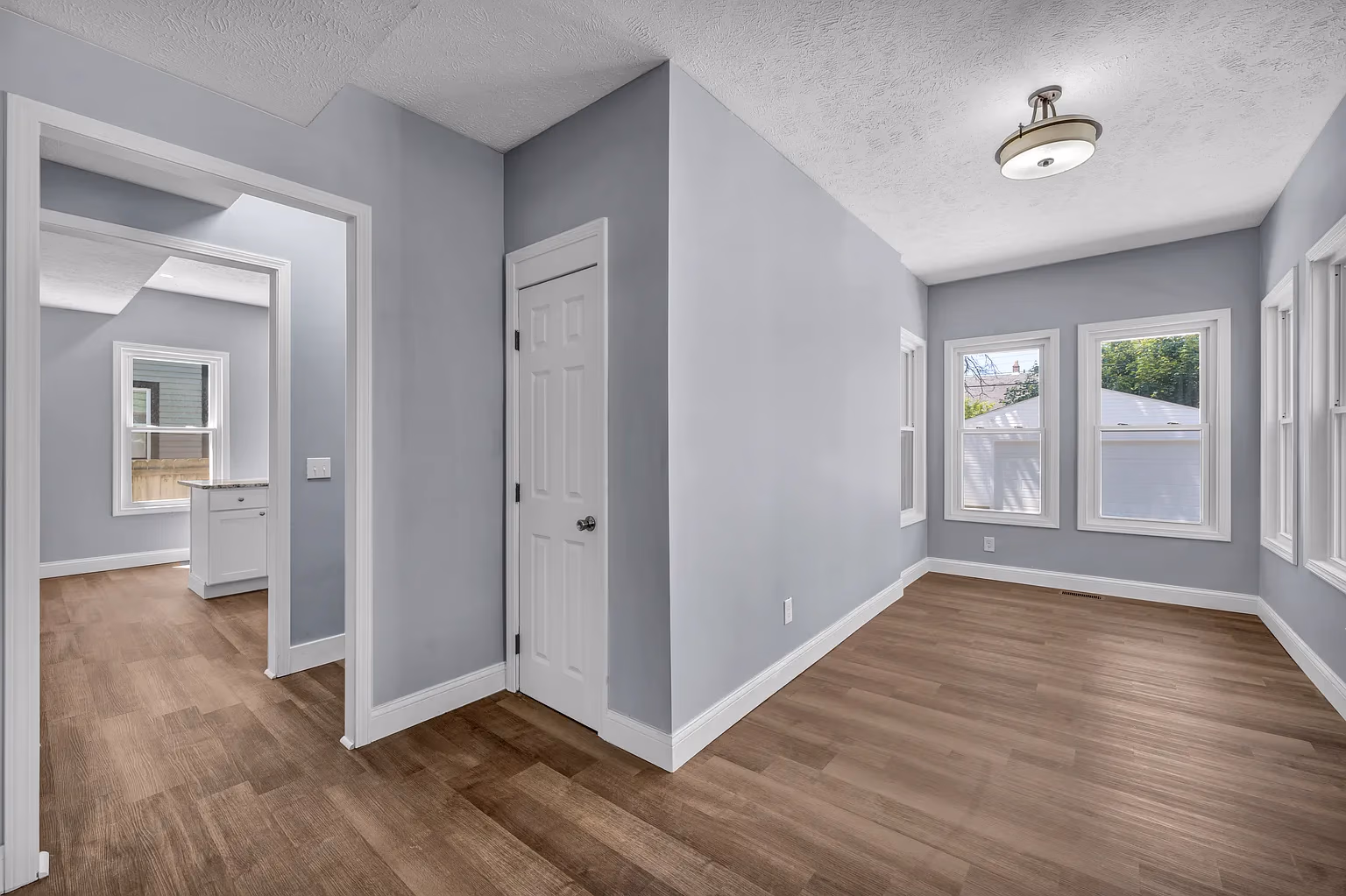 Empty room with wood floor, gray walls, white trim, three windows, ceiling light, and an open doorway.